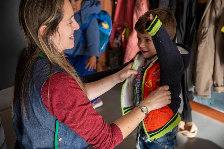 Maestra ayudando a un niño a ponerse la campera en un centro educativo