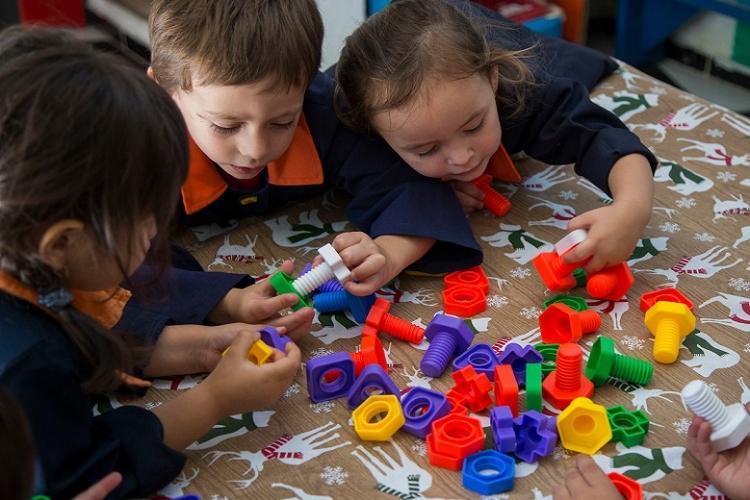 Tres niños juegan en una mesa con jueguetes de encastre en su jardín de infantes