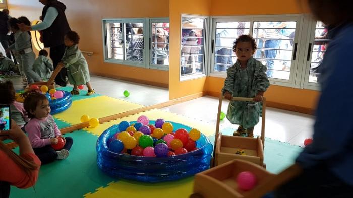 2 niños juegan en salón de CAIF. Se ve su reflejo en el espejo. Están sobre una alfombra de colores.