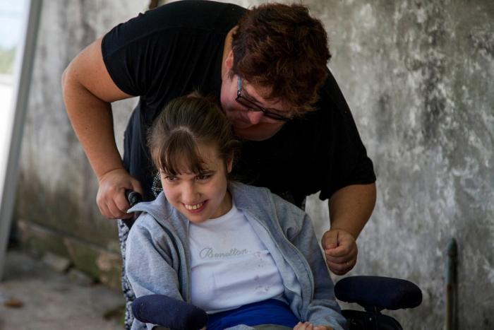 Asistente personal empuja silla de ruedas de su niña asistida. Ambas sonrien.