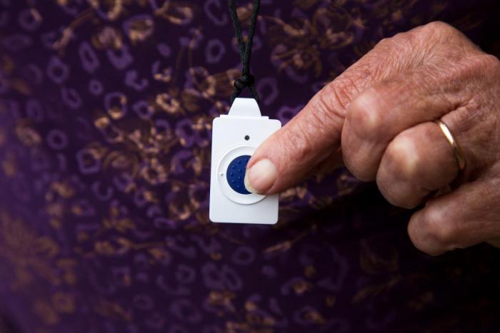 Plano detalle de mujer mayor presionando el botón de teleasistencia en casa