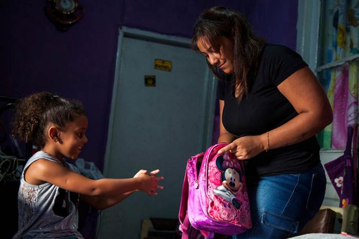 Joven preparándose para ir al liceo junto a su hija pequeña