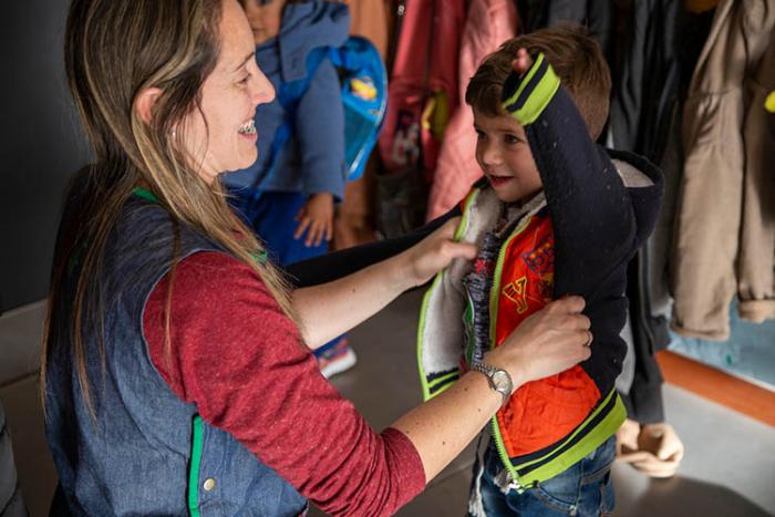 Cuidadora en centro Caif ayuda a un niño a ponerse la campera antes de salir Cuidadora en centro Caif ayuda a un niño a ponerse la campera antes de salir