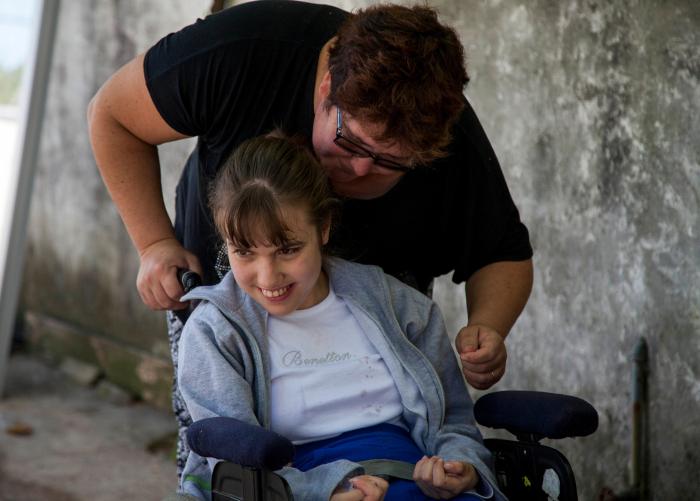 Lanzamiento de Cursos de Atención a la Dependencia Mujer hablando con niña sentada en silla de ruedas, que se ríe.