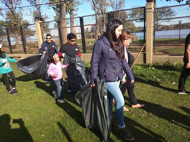Hombres, mujeres y niños voluntarios recorren un espacio público con bolsas de residuos y juntan deshechos