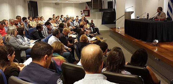 Fotografía del público asistente al encuentro. En el escenario, el director nacional brindando unas palabras