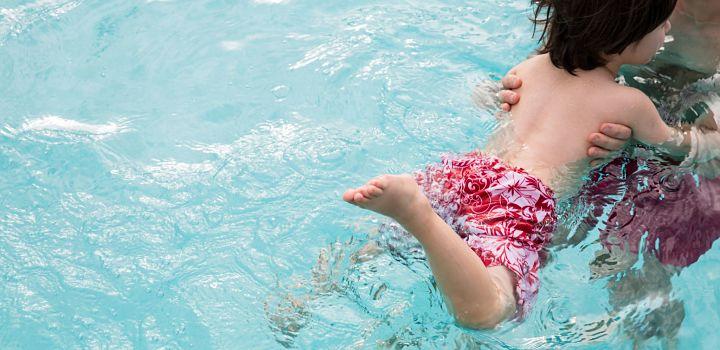 Niño nadando en piscina, en brazos de un adulto