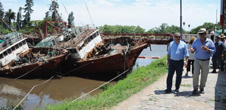 Barco semi hundido, autoridades caminando por la calle del costado