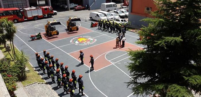 Fotografía de bomberos en formación, en el cuartel de bomberos, con la maquinaria donada detrás 