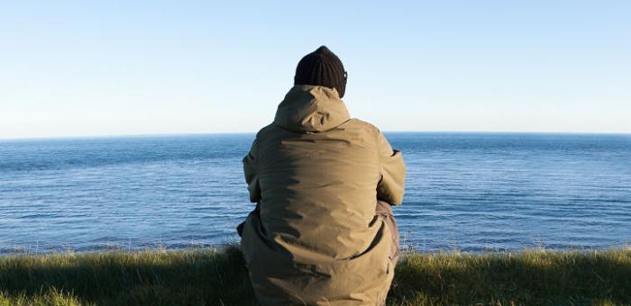 Hombre al aire libre, muy abrigado mirando al mar. 