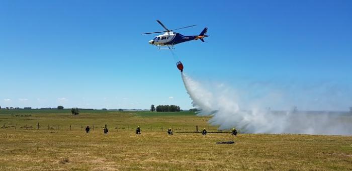 Helicoptero haciendo una descarga de agua, cerca de los bomberos, en un entrenamiento