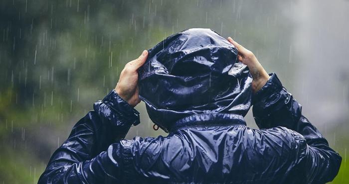Persona de espaldas poniéndose la capucha de la campera de lluvia bajo una tormenta