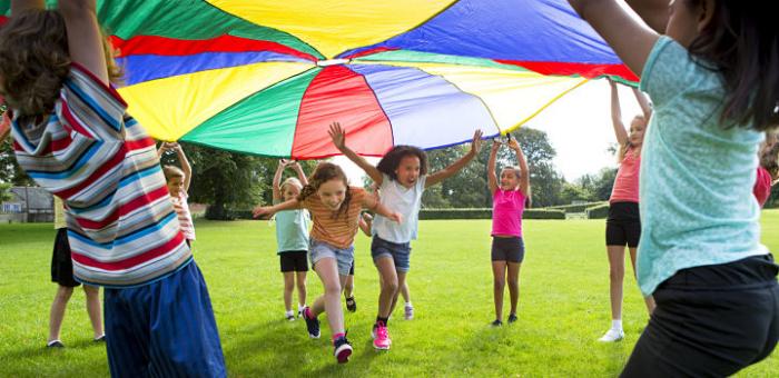 Niños y niñas jugando en el pasto con una tela de colores