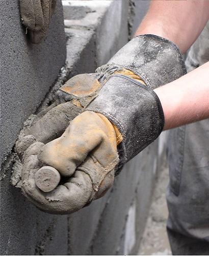manos con guantes de construcción colcando un ladrillo en una pared