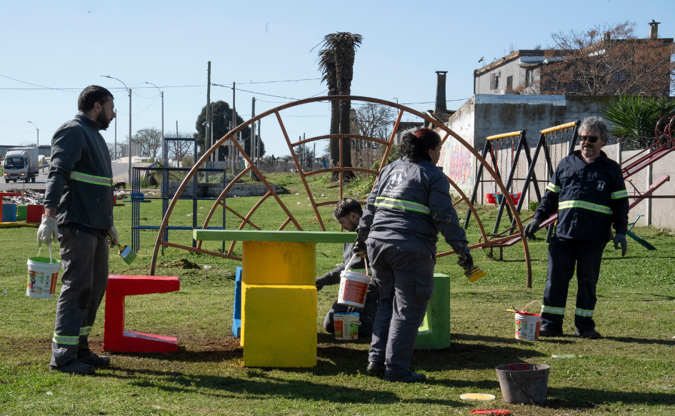 Tres funcionarios de la Intendencia de Canelones pintan equipamiento en una plaza de Las Piedras
