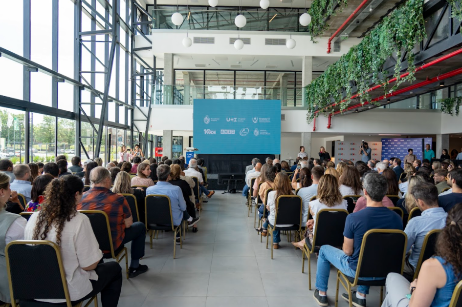 Audiencia sentada frente a un escenario con una pantalla gigante