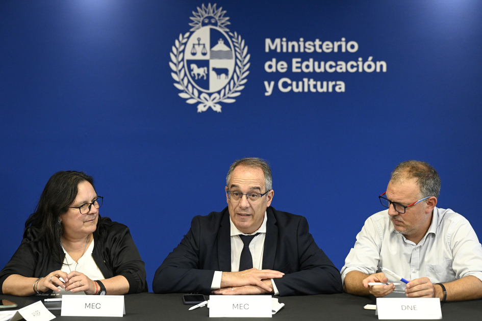 Tres personas sentadas con brazos apoyados sobre la mesa.