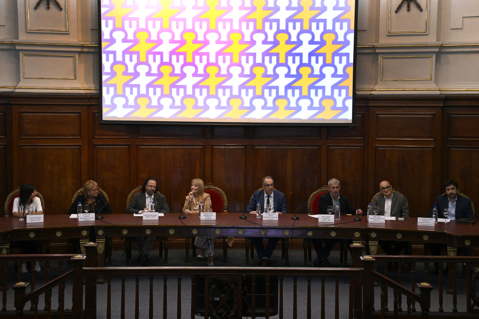 Ocho personas sentadas en la mesa de la oratoria con una pantalla al fondo.