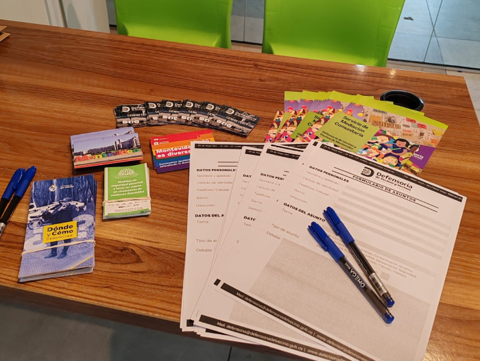 Materiales informativos y formularios de reclamo de la Defensoría sobre una mesa.