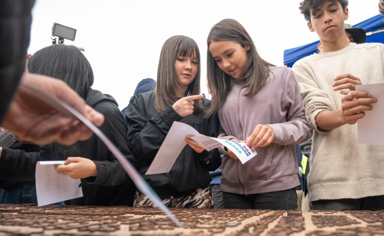Tres adolescente integrantes de Ni Silencio Ni Tabú pegan stickers en una maqueta de Cerro Norte