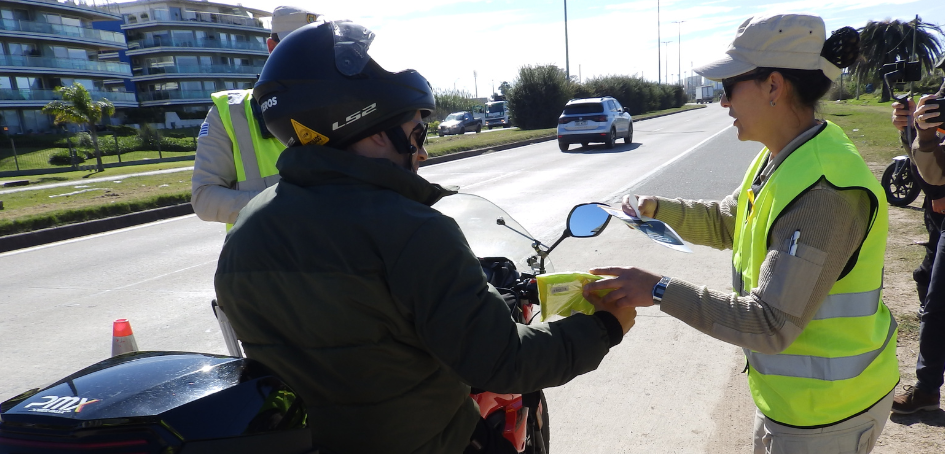 Agente de Policía Caminera entrega chaleco reflectivo a motociclista Agente de Policía Caminera entrega chaleco reflectivo a motociclista