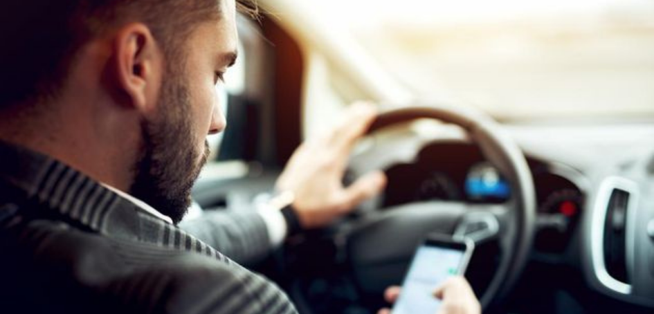 Conductor con una mano en el volante y la otra manipulando un teléfono celular Conductor con una mano en el volante y la otra manipulando un teléfono celular