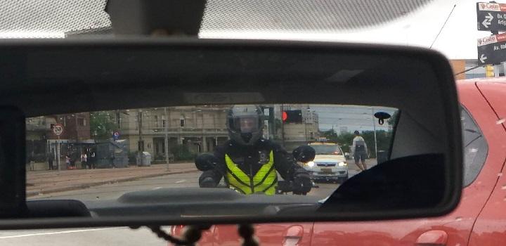 Vista de motociclista con casco e indumentaria reflectiva en espejo retrovisor de auto Vista de motociclista con casco e indumentaria reflectiva en espejo retrovisor de auto