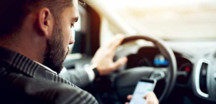 Conductor con una mano en el volante y la otra manipulando un teléfono celular